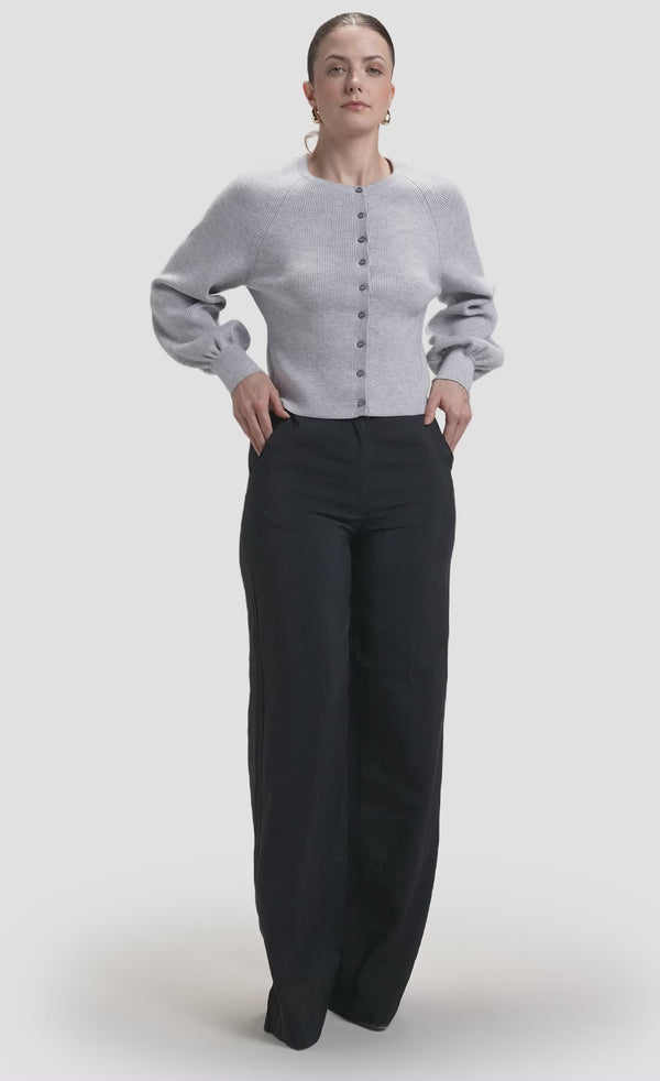 Model wearing grey ribbed knit button cardigan with balloon sleeves over black wide-leg trousers 
